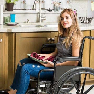 A woman holds a notebook in her kitchen. She is using a wheelchair