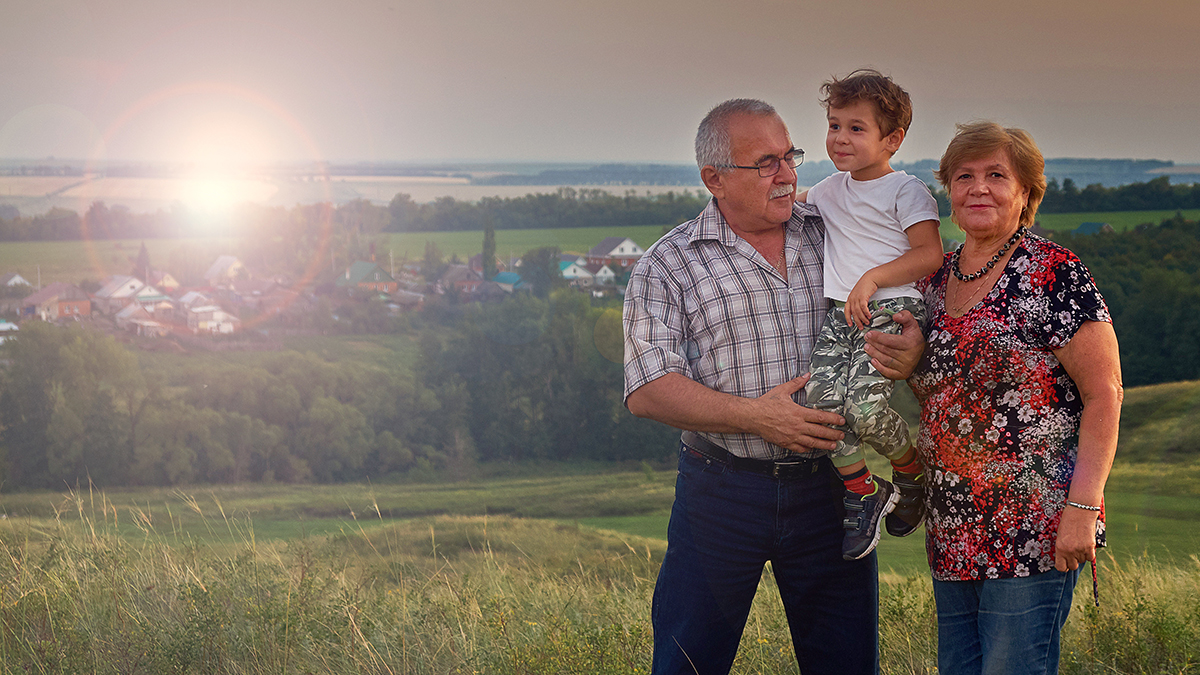 grandparents holding a small boy on a hill overlooking a small town