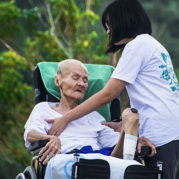 Outdoor scene of woman providing care to an elder who is sitting in a wheelchair