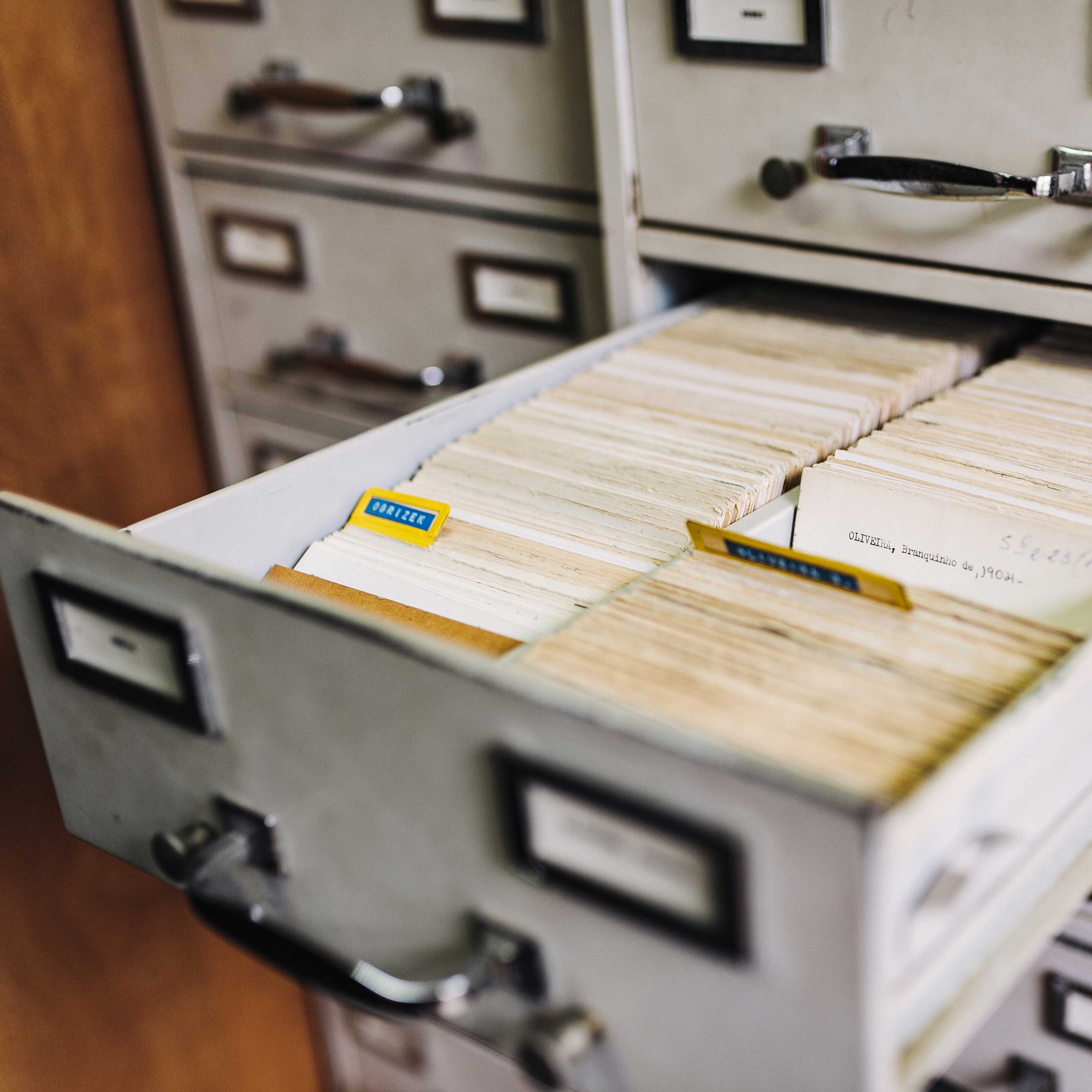 A file drawer is open in a tall white file cabinet, showing index cards inside