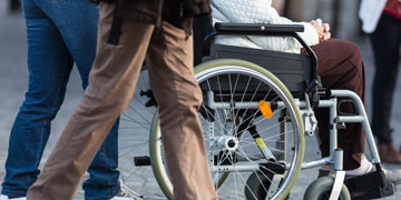 person in a wheel chair being pushed on a busy sidewalk