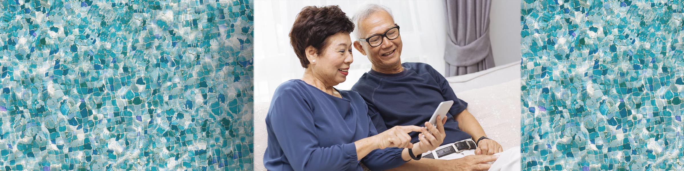 Elder Asian couple sitting on a couch, looking at a mobile phone together